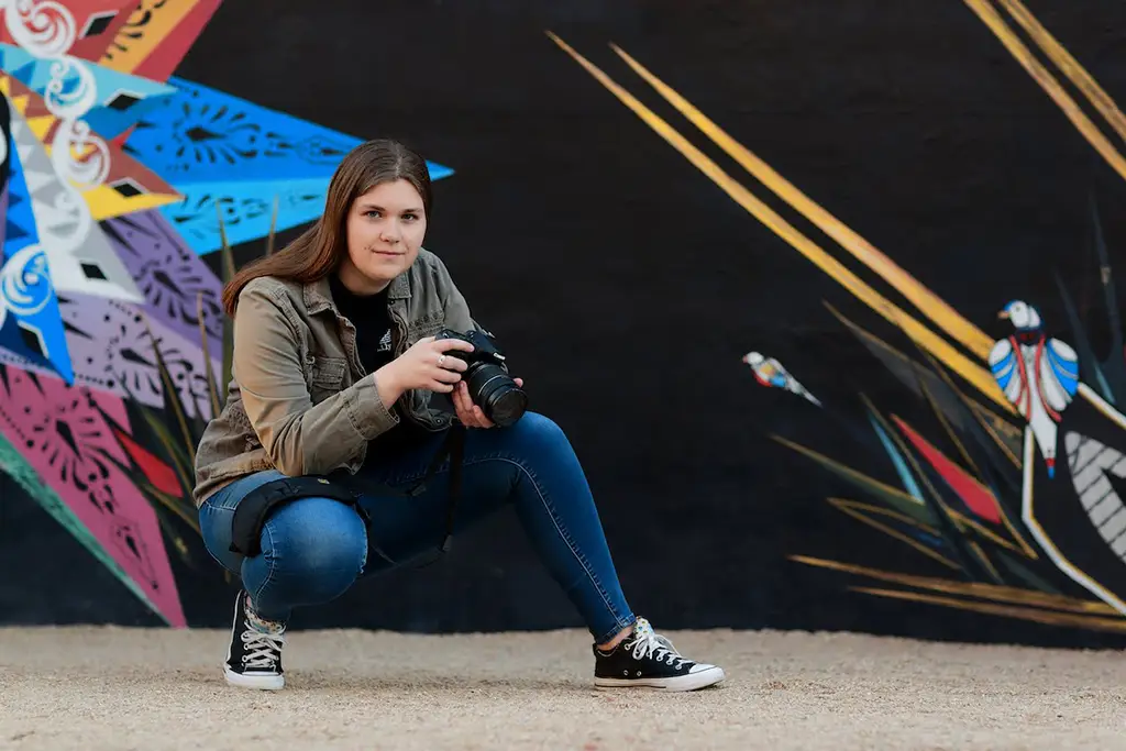 Me, crouched with a camera in front of a colorful mural